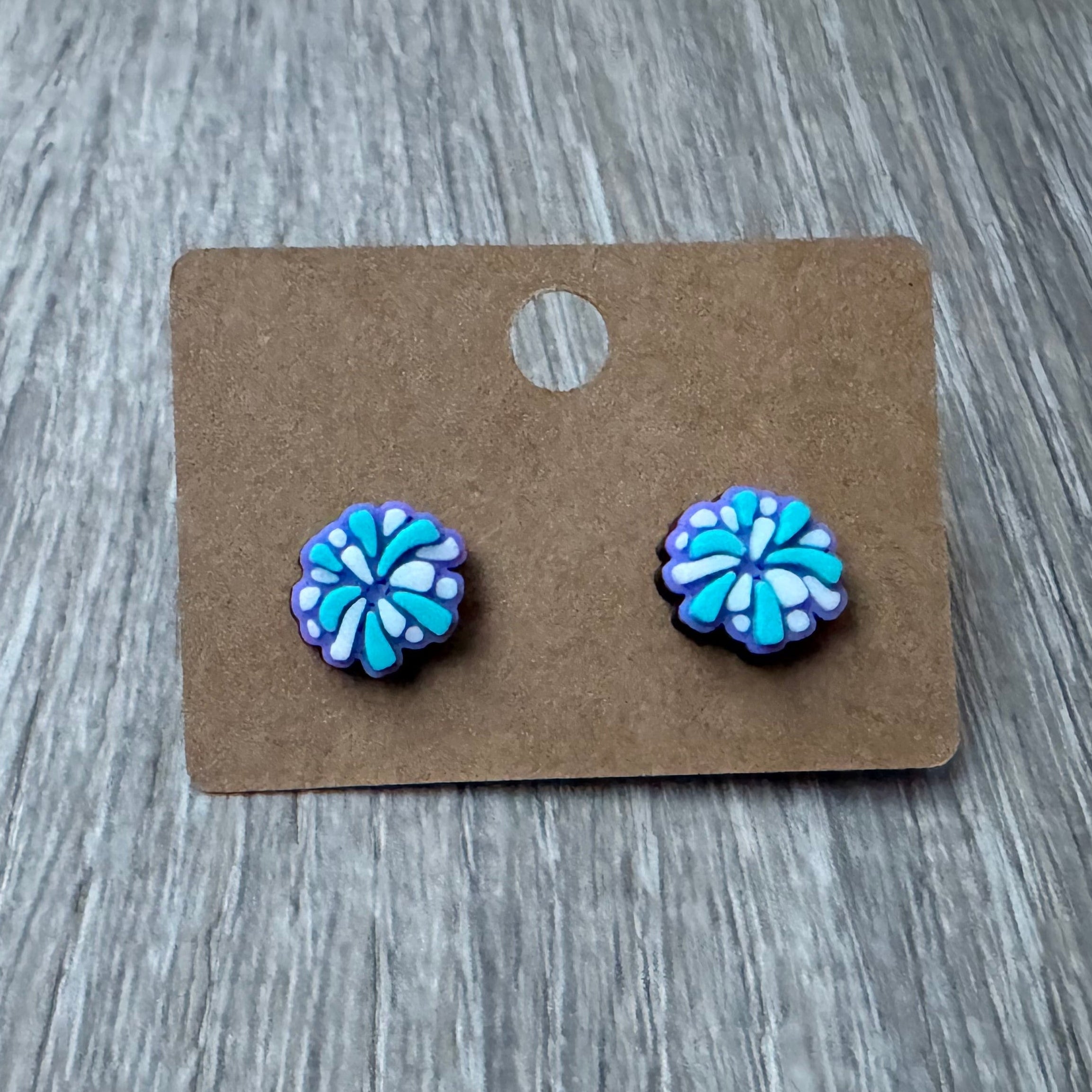 PomPom earrings on a cardboard backing with a wooden surface background