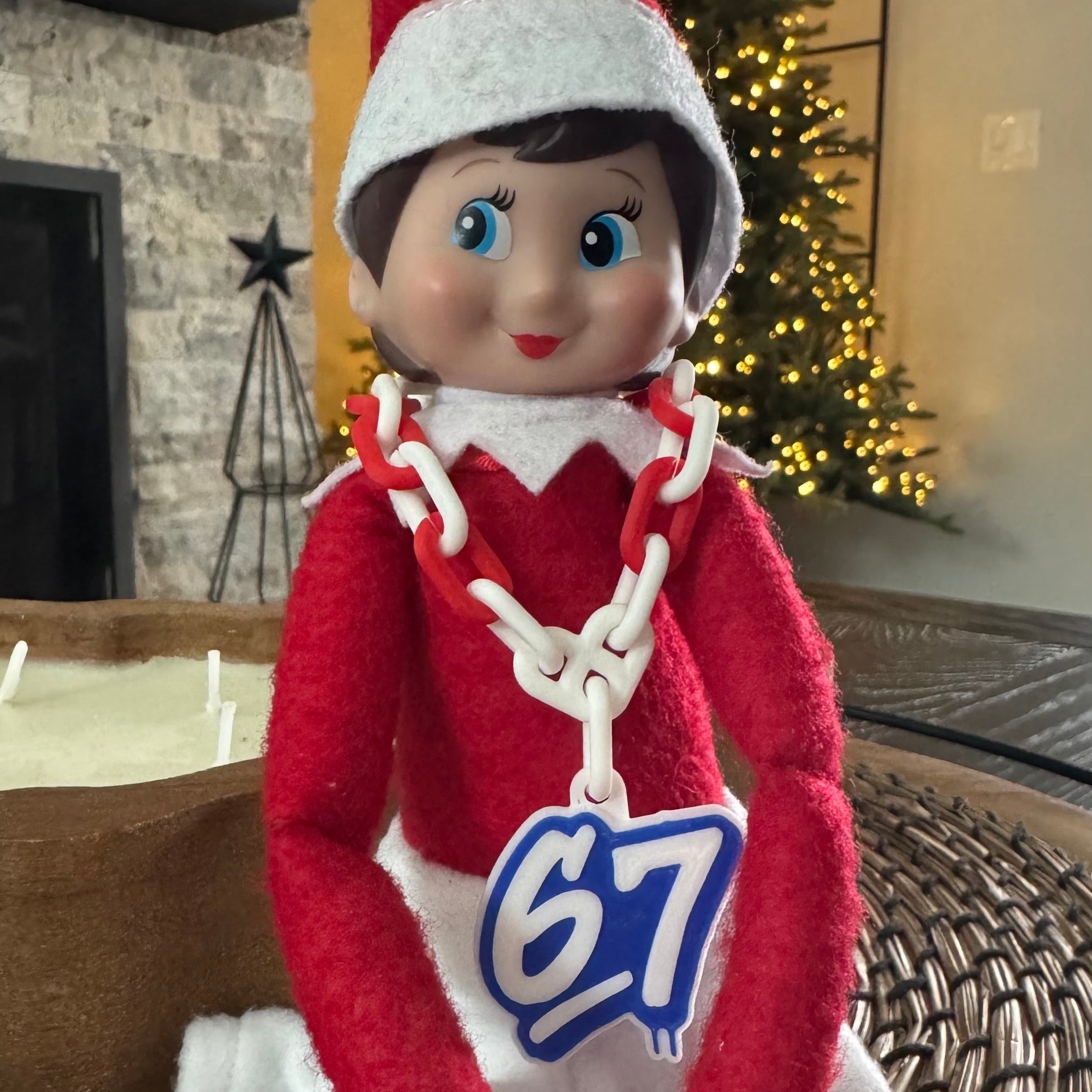 Elf on the Shelf with a hype chain sitting in front of a Christmas tree.